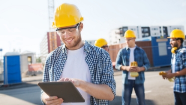Construction worker smiling on his iPad with his coworkers talk behind him